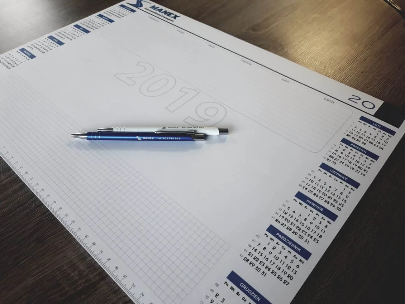 długopisy z nadrukiem Manex na tle podkładów na biurko